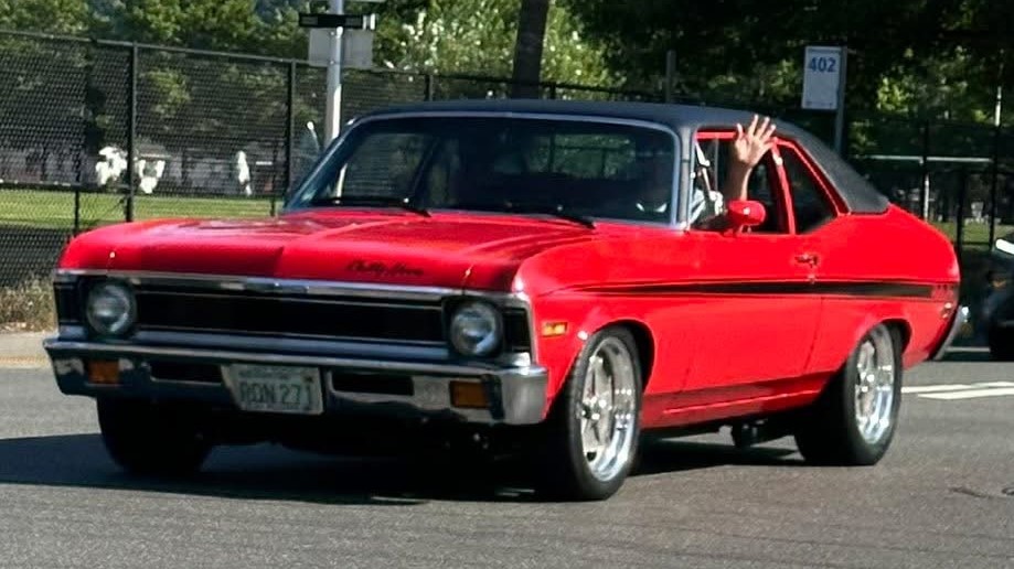 man waving from diver's seat of a 1971 Chevy Nova